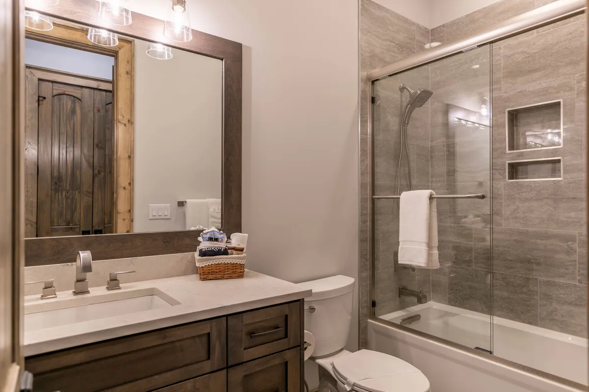 A modern ensuite bathroom with a double sink granite vanity, large mirror, glass shower enclosure, and textured wall tiles. The space feels bright, clean, and luxurious, capturing the spa-like experience mentioned in the text.