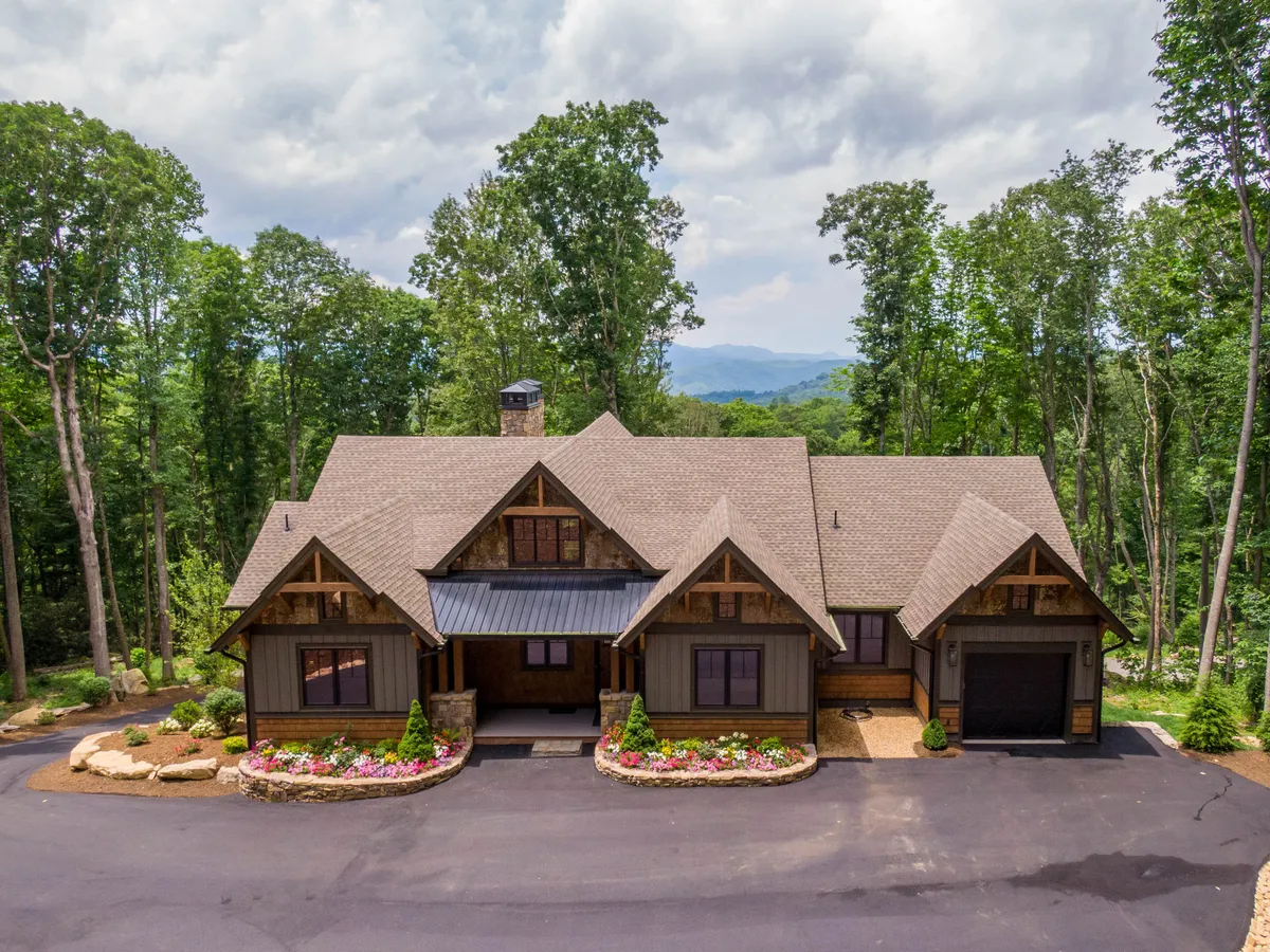 A welcoming view of the main entrance to a cabin, featuring decorative stonework, landscaped gardens with colorful flowers, and warm wooden accents on the porch. The scene is serene, inviting, and highlights the comfort of returning to a private sanctuary after a day of adventure.