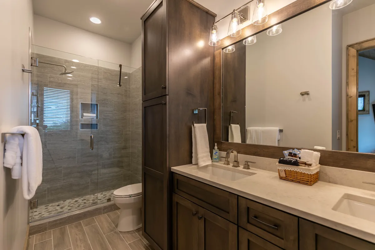 A contemporary bathroom with a glass shower, double sink vanity, mirrored cabinet, and elegant wood cabinetry. The serene design and modern fixtures convey relaxation and convenience.