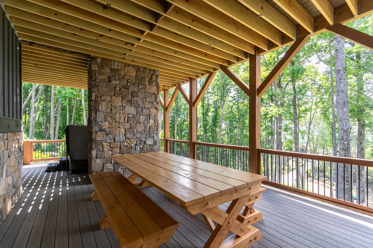 An inviting exterior shot of a wooden picnic table set atop a stone patio, surrounded by tall trees. The space is ideal for family barbecues, casual outdoor meals, and group gatherings in a peaceful, natural setting.