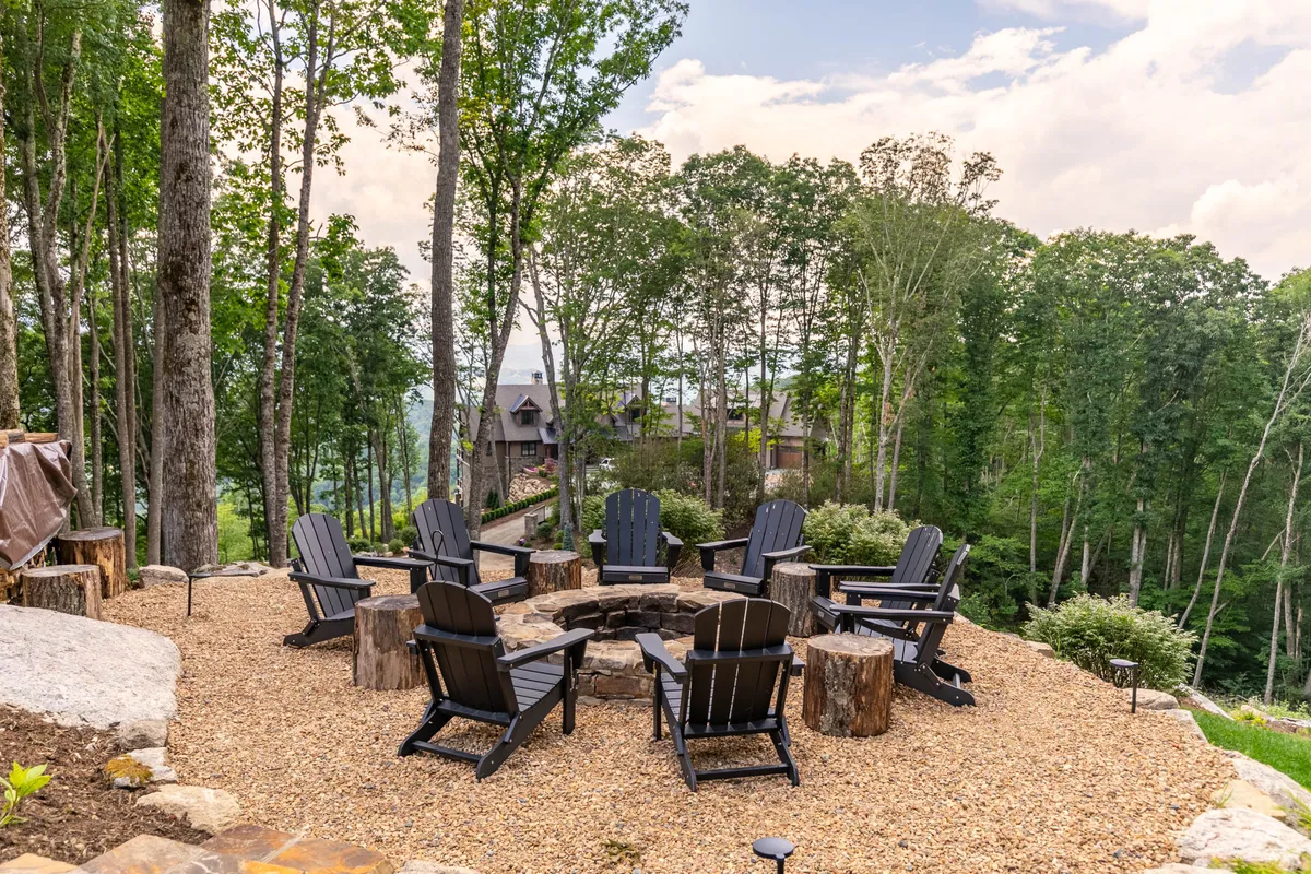 An inviting fire pit encircled by Adirondack chairs sits among lush trees, creating a cozy gathering spot for storytelling, stargazing, and sharing meals outdoors.