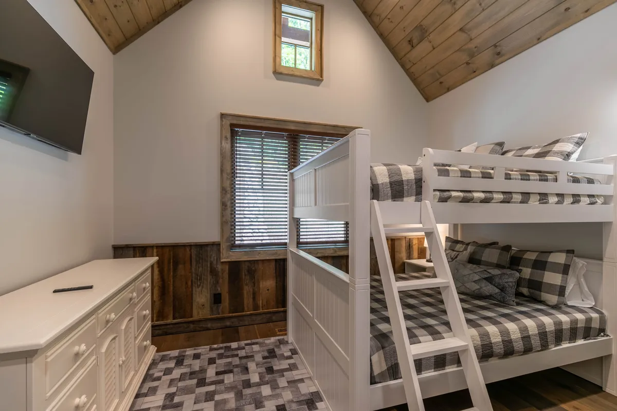 A cheerful bunkroom with a sturdy queen-over-queen bunk bed, a window letting in natural light, and a dresser for storage. The room is inviting and well-suited for kids or additional guests, offering both comfort and practicality.