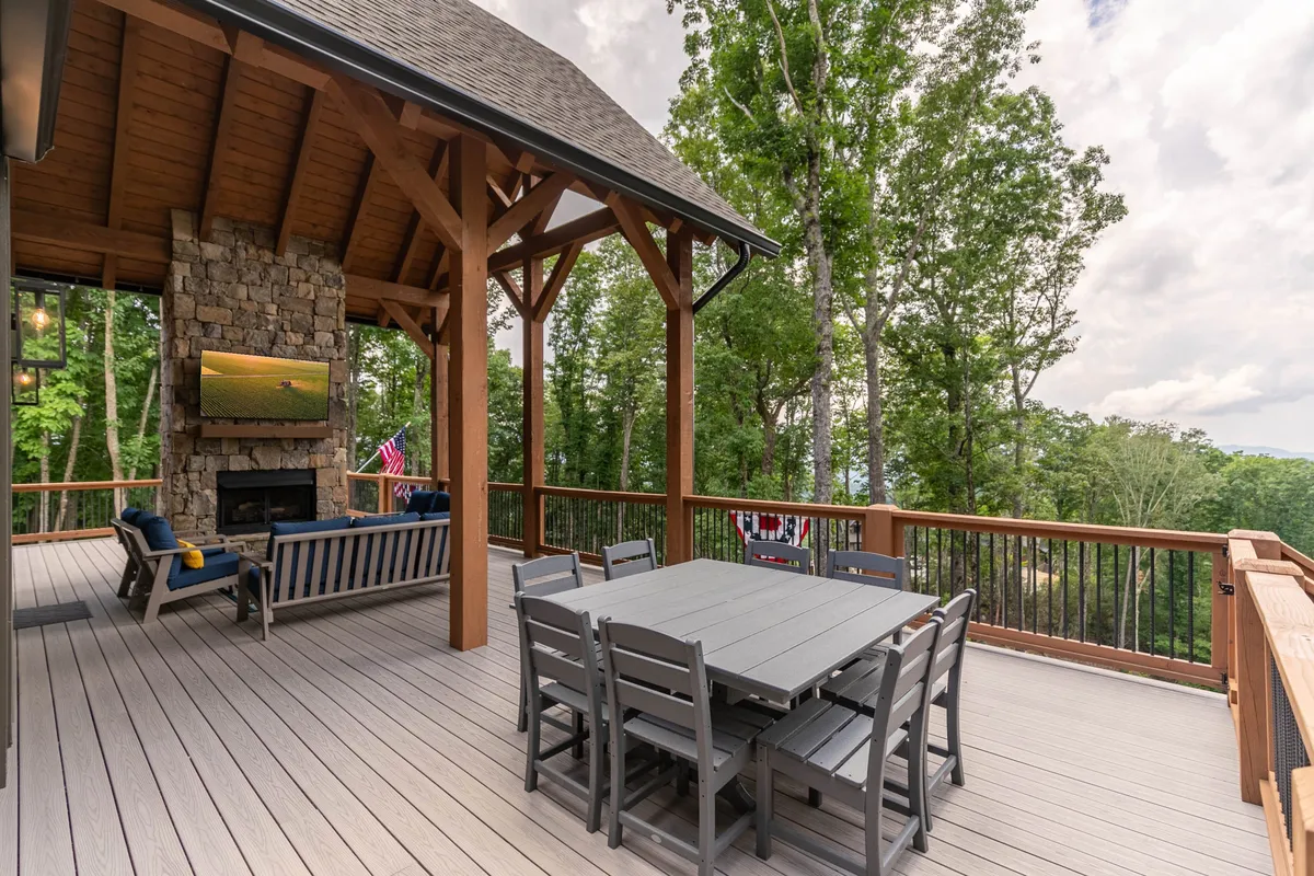 An outdoor seating area with a dining table, stone fireplace, TV, and surrounding trees, blending the comforts of home with the adventure of being outdoors. The setup invites guests to dine, socialize, or relax while immersed in nature.